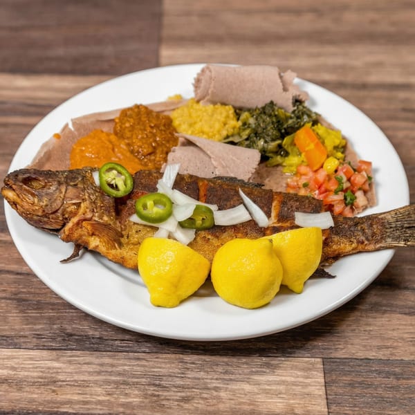 Whole fried fish with injera, various stews, and lemons on a white plate.