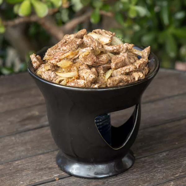 Savory beef and onions in a black ceramic bowl on a rustic wooden table.