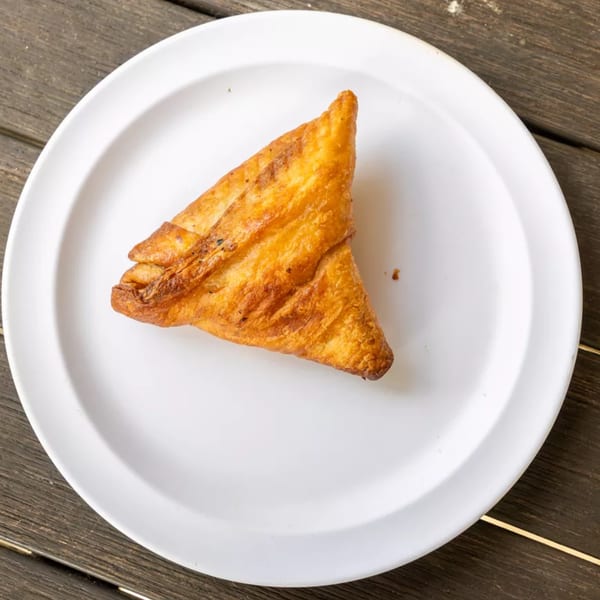 Golden brown triangular pastry on a white plate, set against a rustic wooden table.