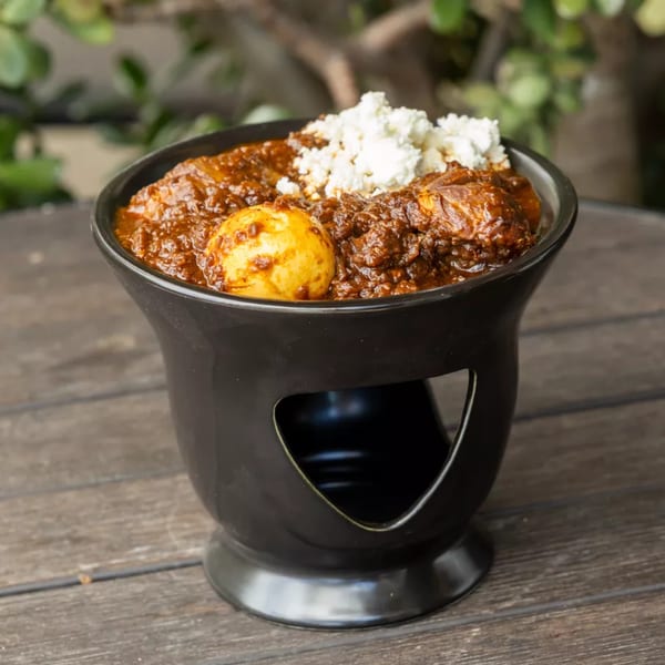 Rich brown curry with a whole boiled egg and crumbled white cheese in a black bowl.
