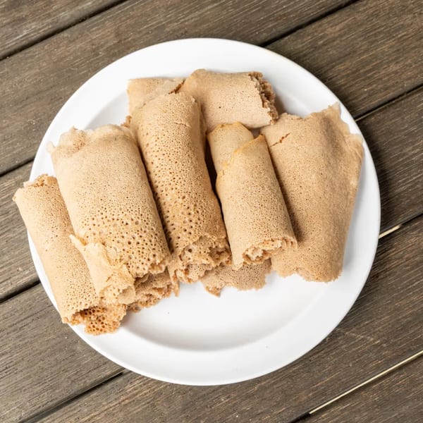 A white plate filled with rolled injera bread, showcasing its spongy texture, on a wooden table.