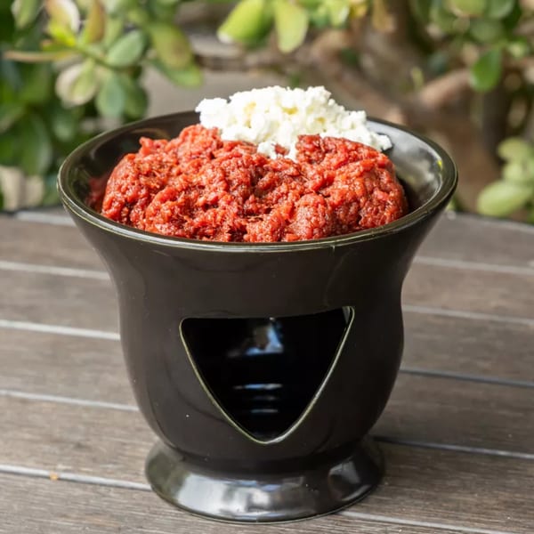 A black bowl filled with red pureed food and a dollop of white cheese on a wooden table.