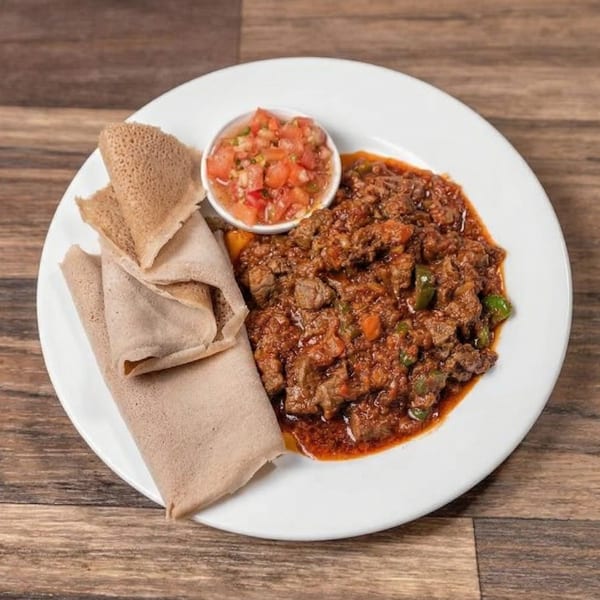 Ethiopian injera bread, spicy meat stew, and tomato salsa on a white plate.
